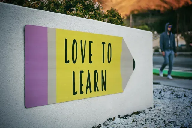 A yellow pencil-shaped sign on a white wall reads 