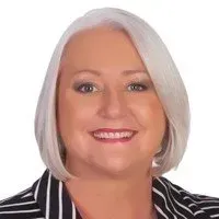 A person with chin-length blonde hair and a friendly smile wearing a black-and-white striped blazer against a white background.