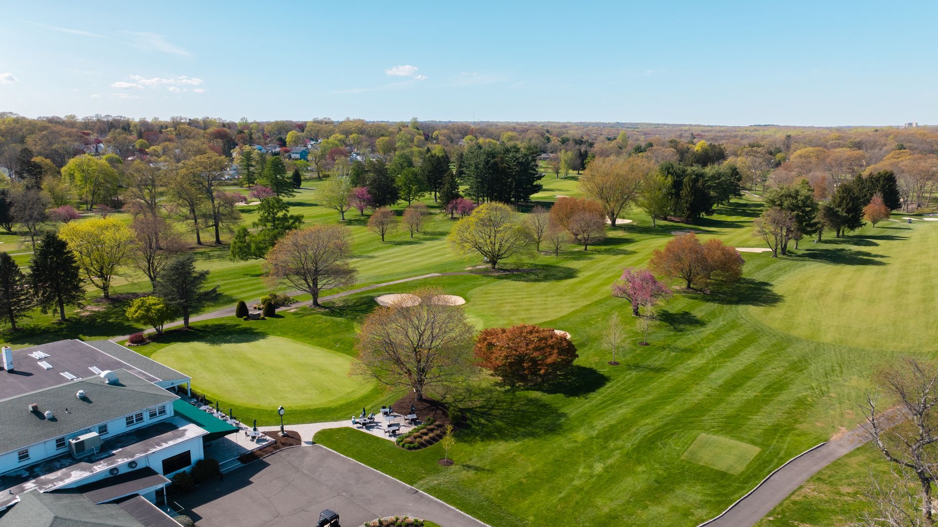 An aerial view of a golf course with trees and a building in the background.
