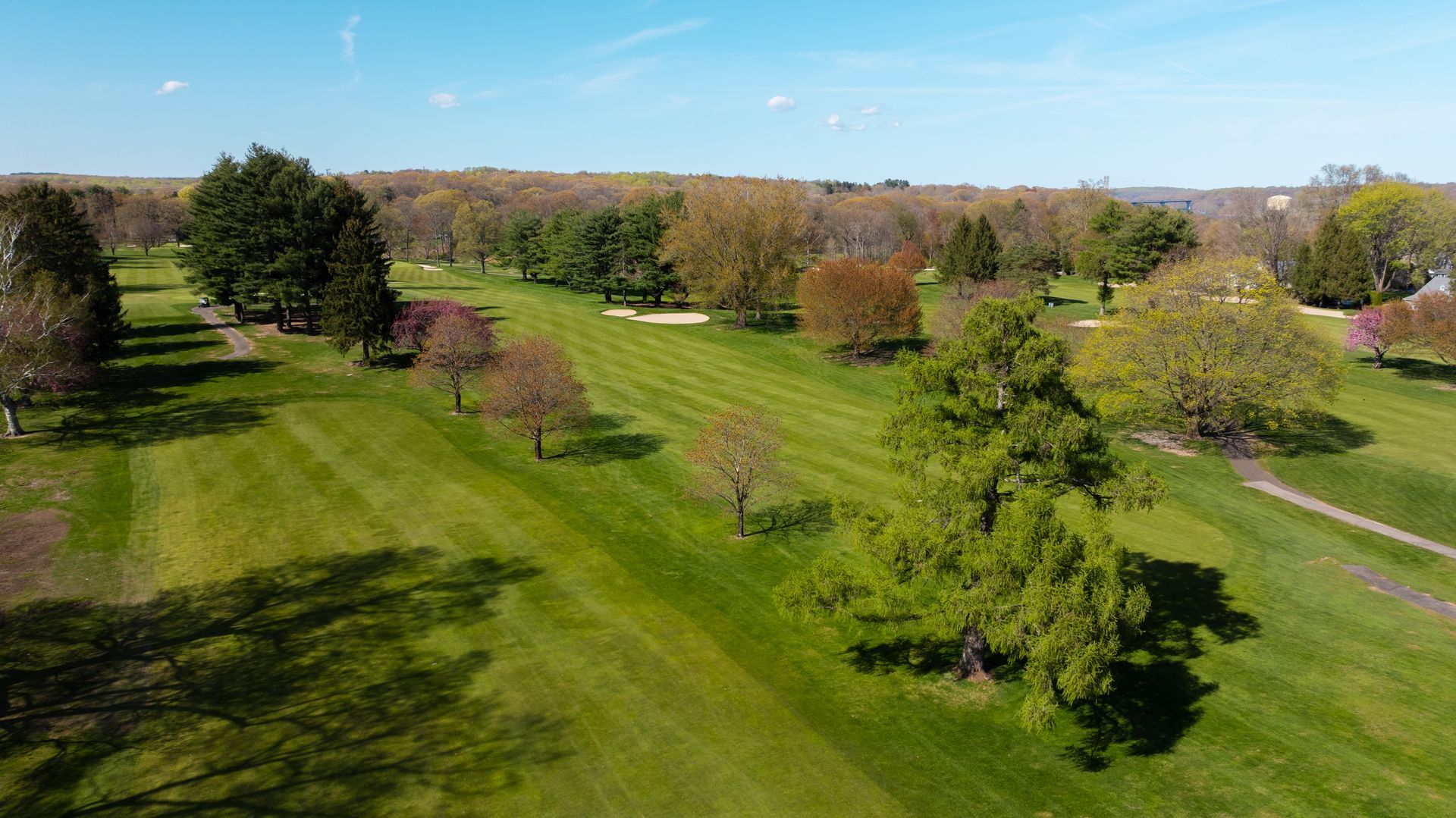 An aerial view of a golf course surrounded by trees on a sunny day.