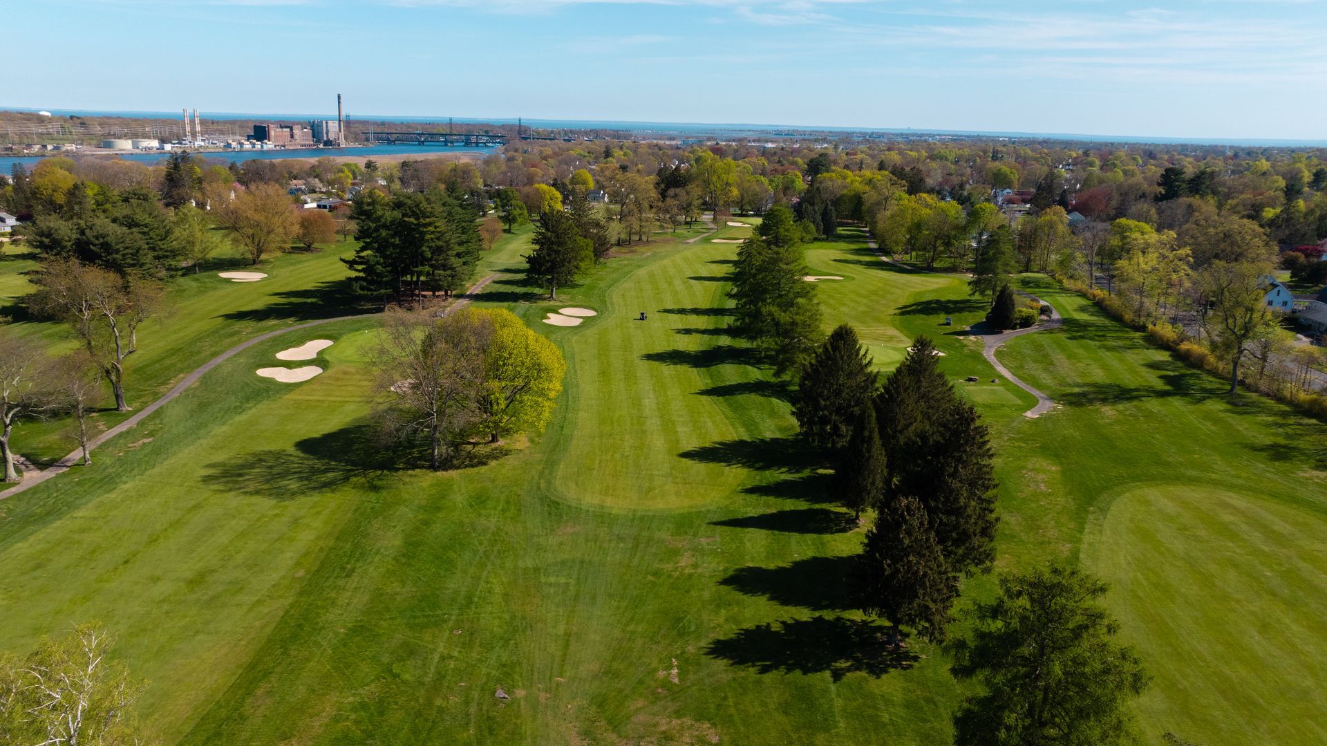 An aerial view of a golf course with trees and a bridge in the background.