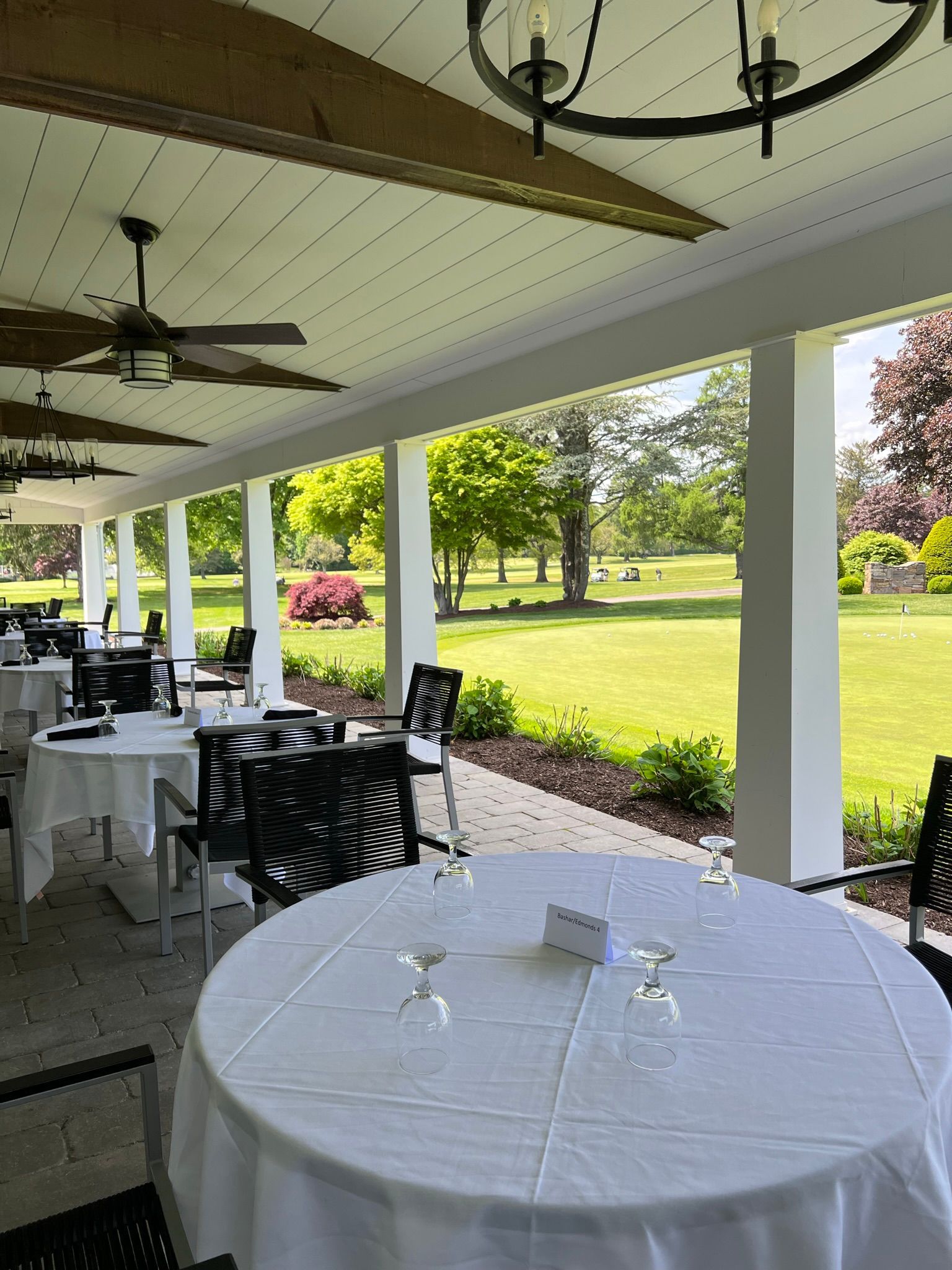 A covered patio with tables and chairs and a view of a park.