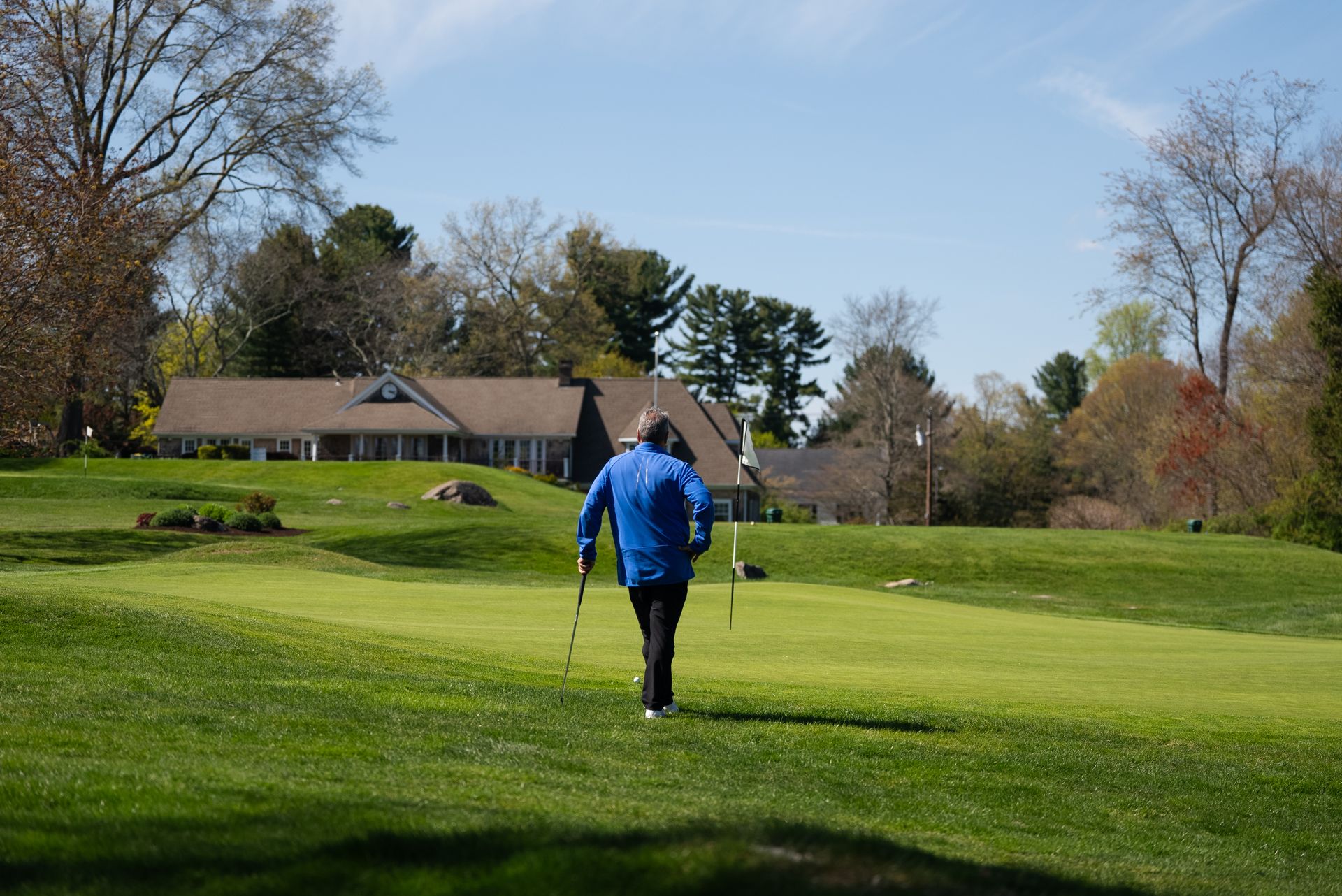 A man in a blue jacket is walking on a golf course.