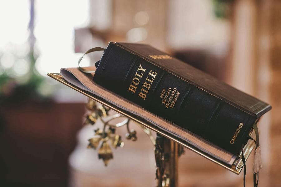 Black Holy Bible resting on a stand, with a small cross charm and warm blurred background