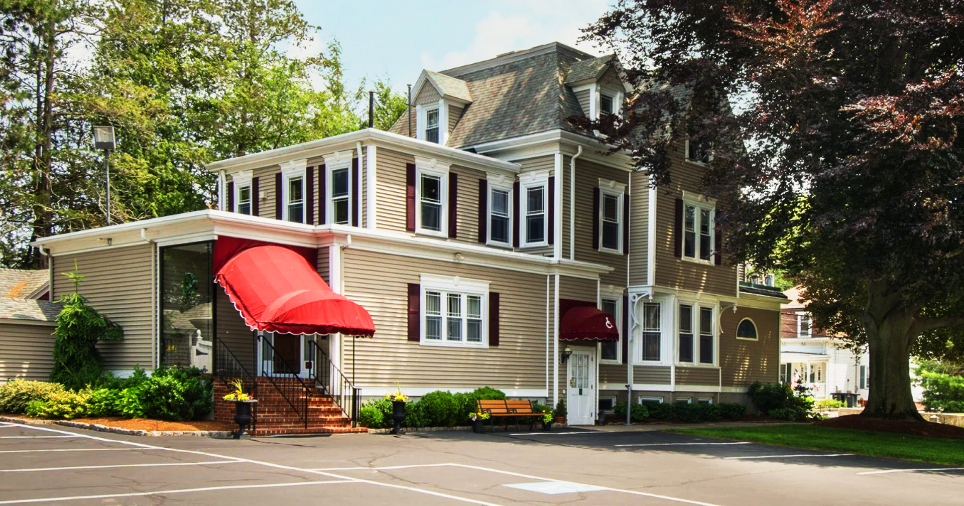 Historic white house with red awning, wraparound porch, and trees along a quiet street
