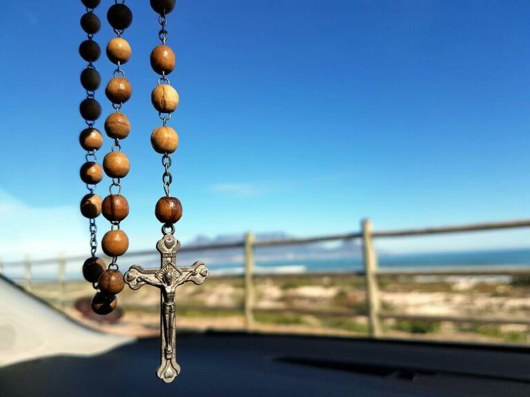 Rosary beads with a crucifix hanging against a blue sky and ocean backdrop