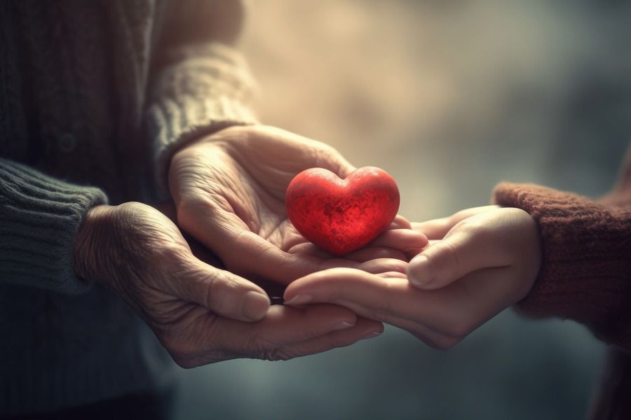 Two hands gently holding a small red heart between them