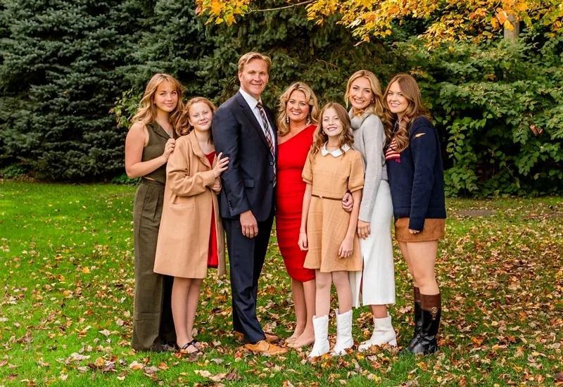 Six people posing together in a leafy garden, dressed in formal and semi-formal outfits.