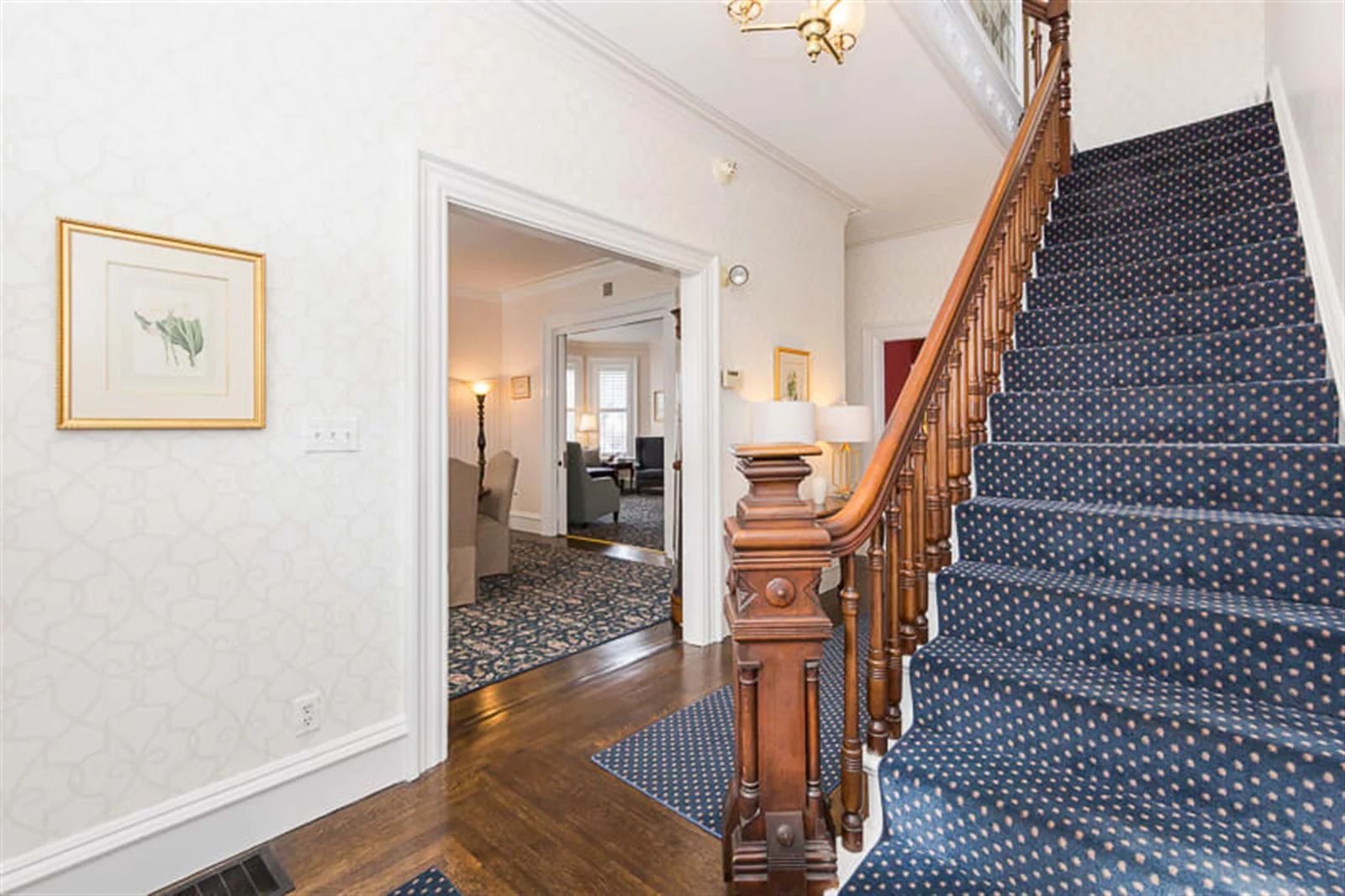 Entryway with blue-carpeted staircase, wooden banister, and view into a dining room through open double doors