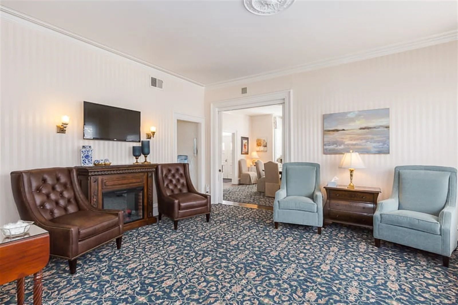 Bright living room with leather and blue armchairs, patterned rug, TV, fireplace, and wall art