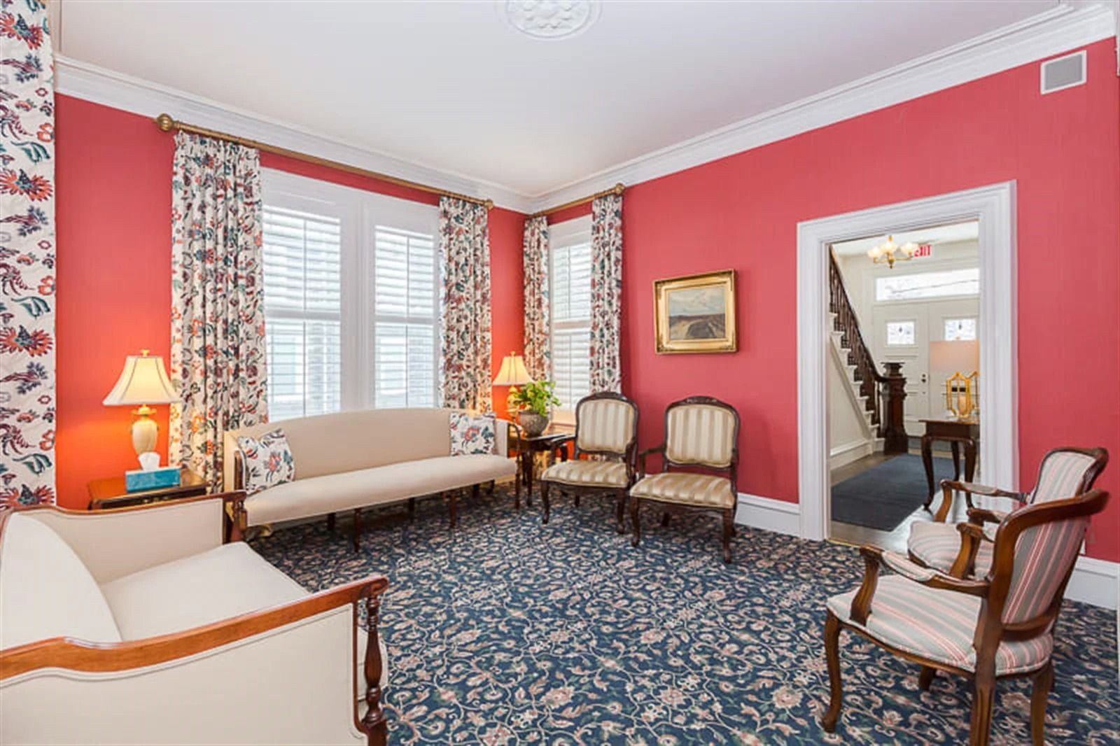 Bright living room with pink walls, blue patterned carpet, beige sofas, and a mirror by a doorway.