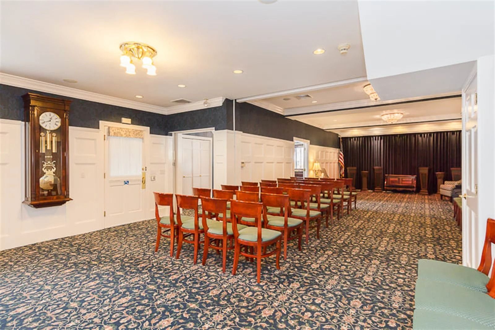 Spacious banquet hall with patterned carpet, wooden chairs, and long tables under bright ceiling lights