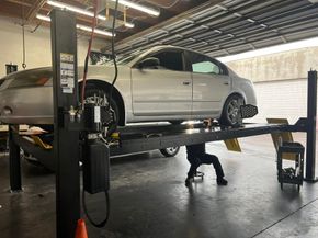 Silver car on a lift in an auto repair shop, with a mechanic working underneath | Miller Auto Repair