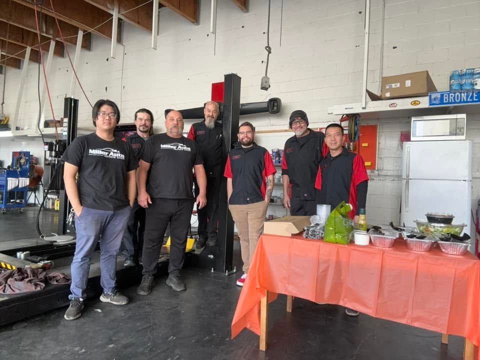 Group of people posing in a workshop beside a table | Miller Auto Repair Shop