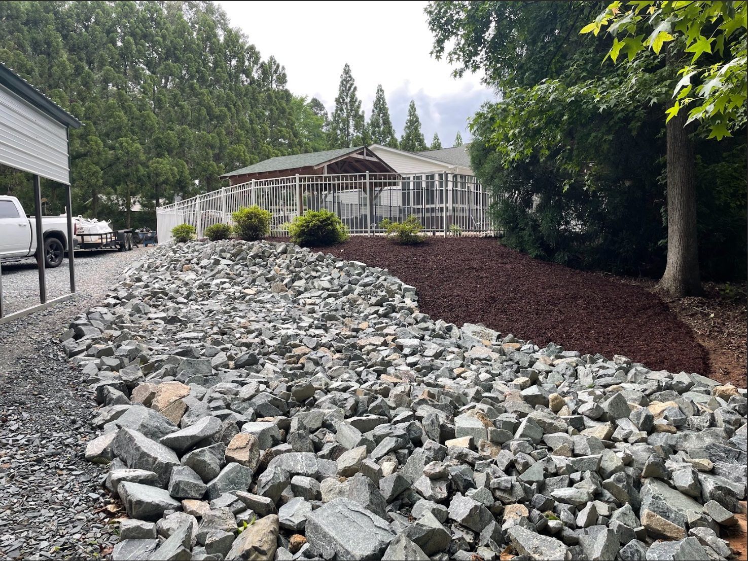 A rock and mulch landscape bed in front of a building with a carport on the left.
