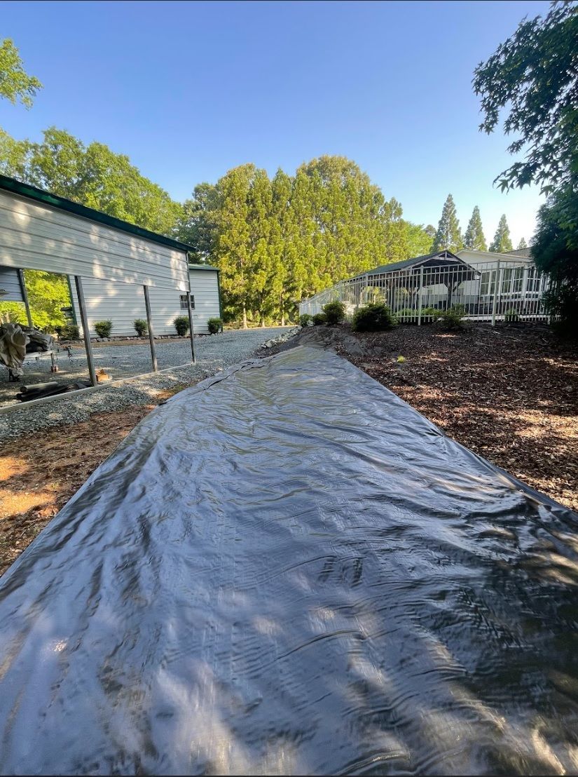 Long gray tarp laid out in a backyard, stretching toward a building and trees under a clear sky.