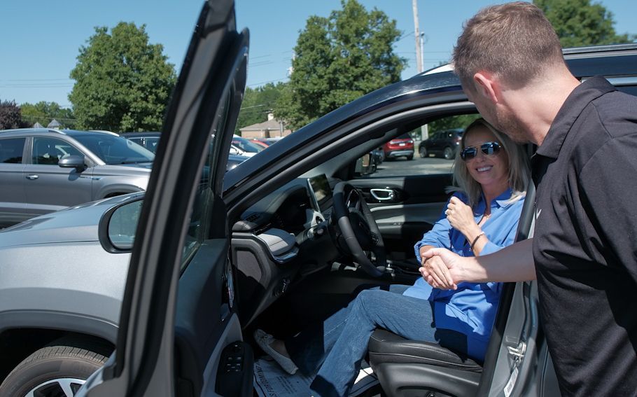 Woman sits in open car door while man leans in and talks to her in a parking lot