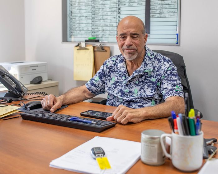 Man seated at a desk in an office, smiling with hands on a keyboard beside a phone and stationery.
