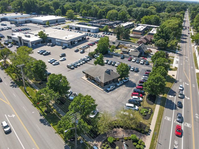 Aerial view of a shopping center parking lot beside a busy road with many parked cars and trees