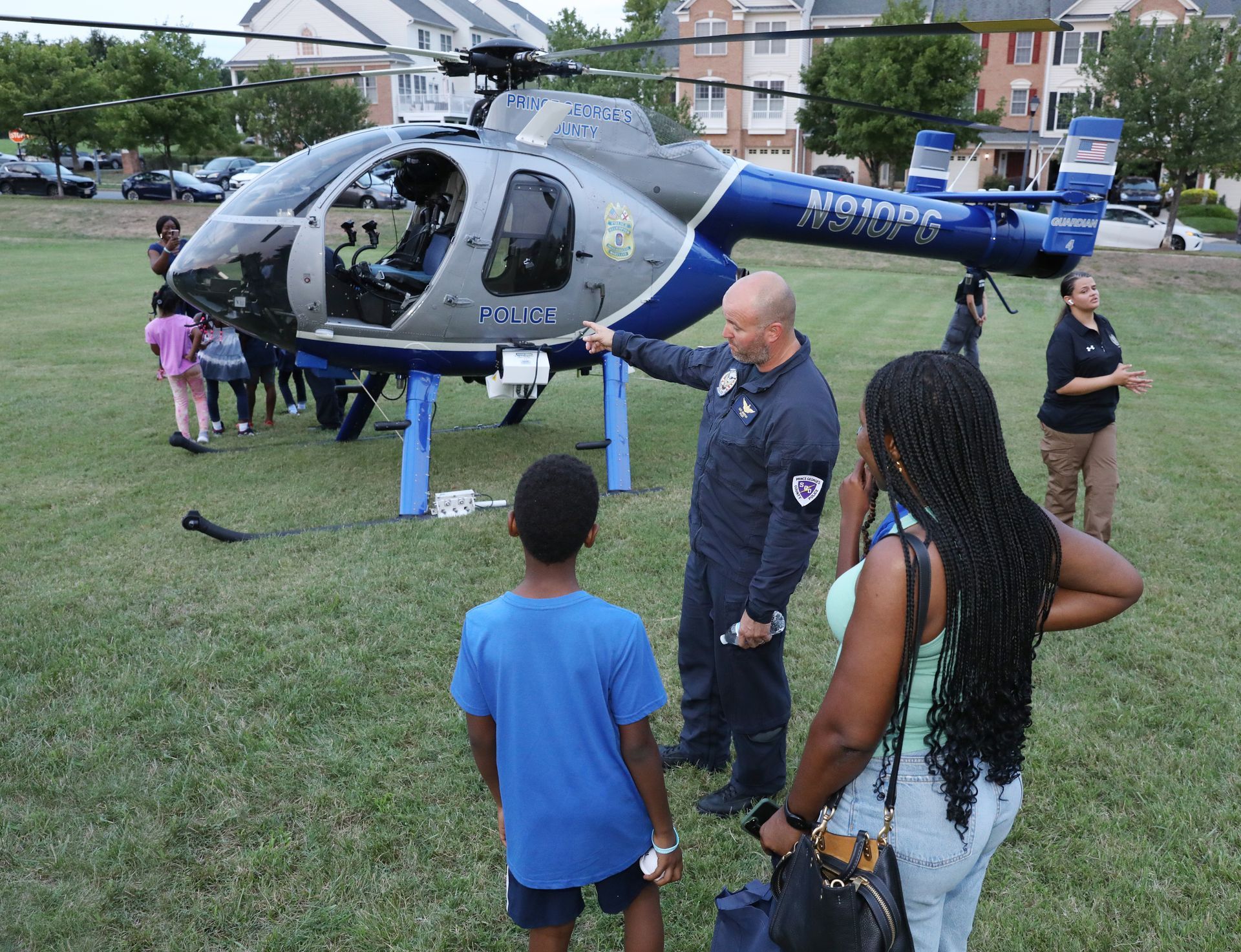 Police helicopter on a grassy field with people gathered around, including a man speaking to children nearby