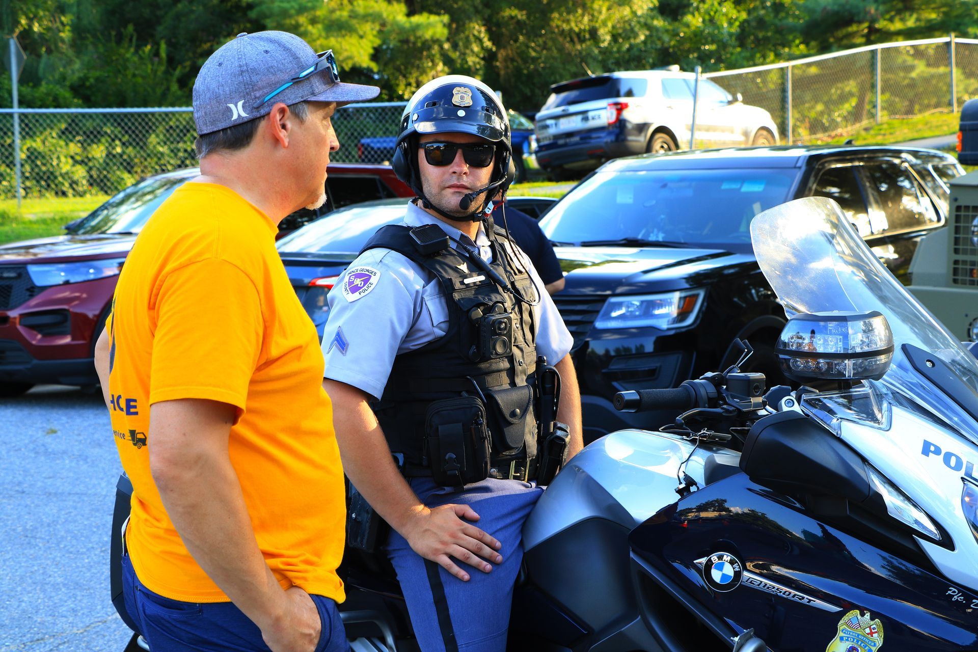 Man in orange shirt talking to police officer beside a motorcycle at a roadside scene