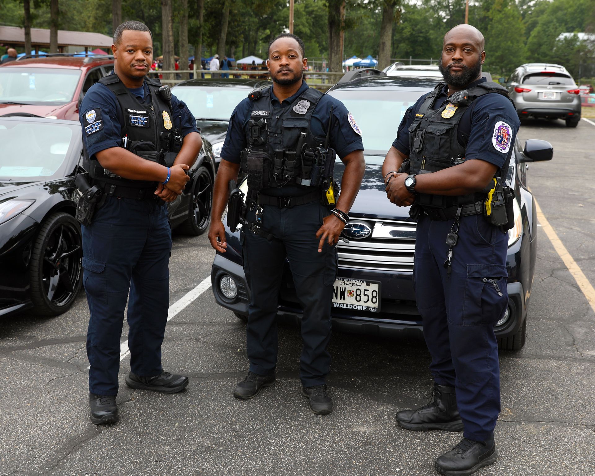 Three police officers standing in front of patrol cars in a parking lot
