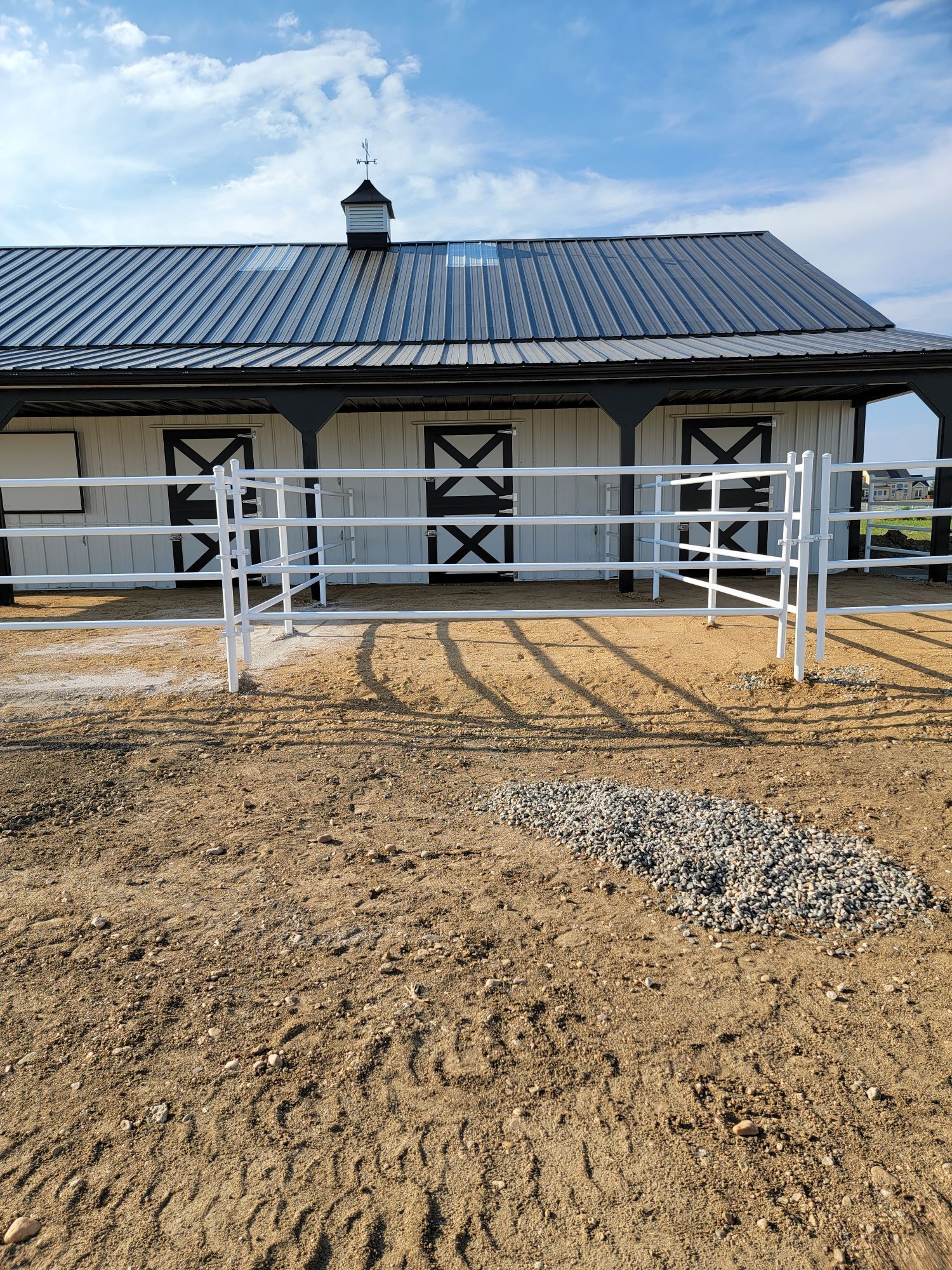 A white barn with a black roof and a white fencebuit by Greater Western Fence in front of it.
