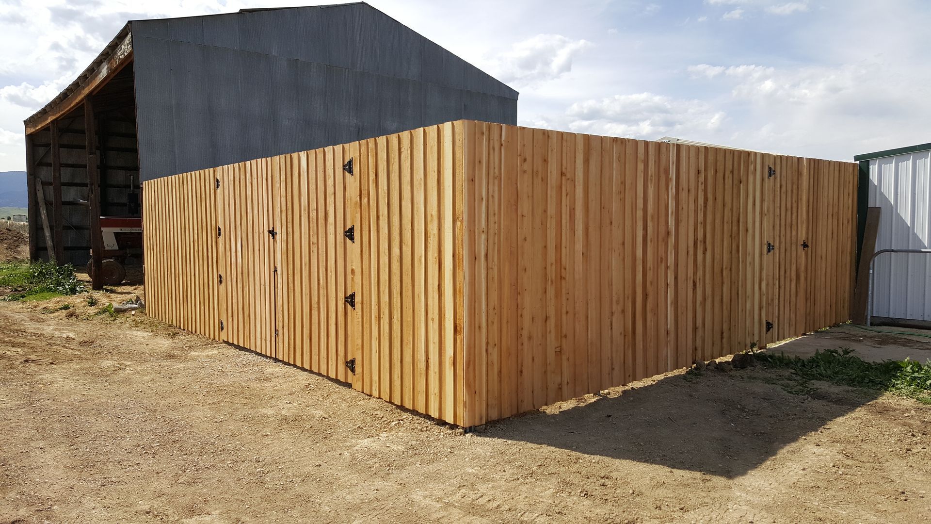 A wooden fence built by Greater Western Fence is sitting in the dirt in front of a barn.