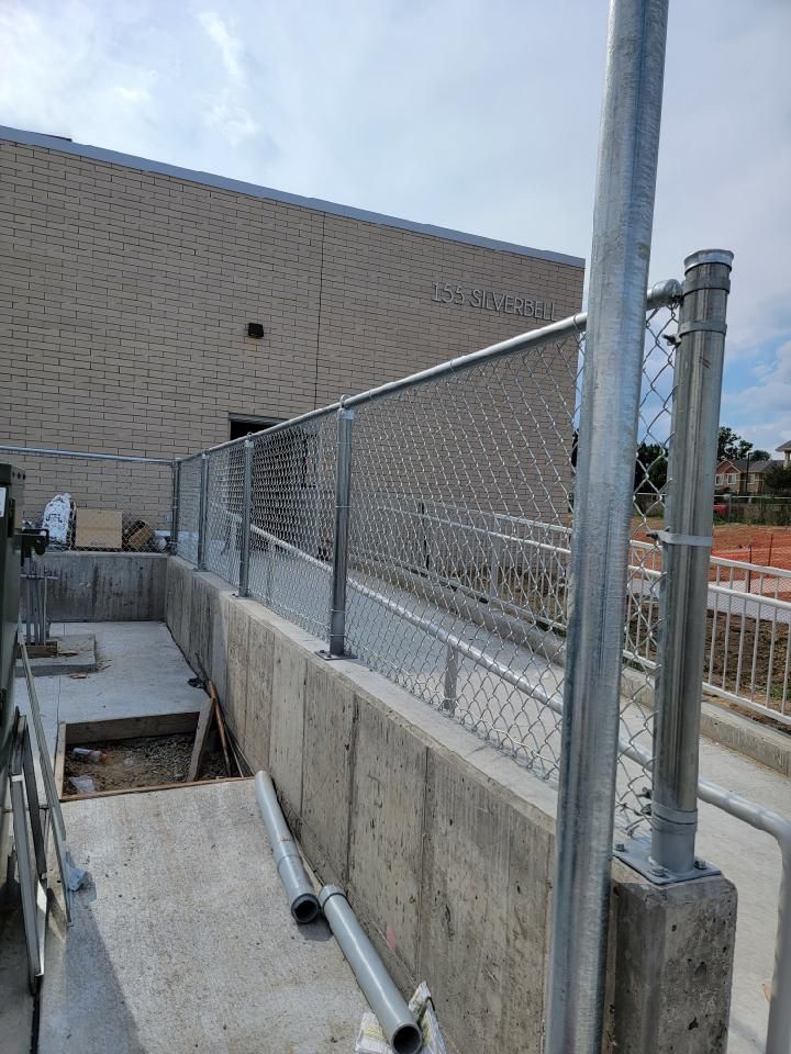 A chain link fence is being buit by Greater Western Fence on the side of a building.