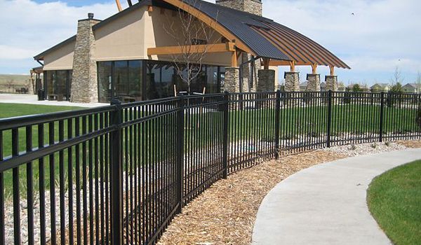 A black fence built by Greater Western Fences surrounds a concrete walkway in front of a house.