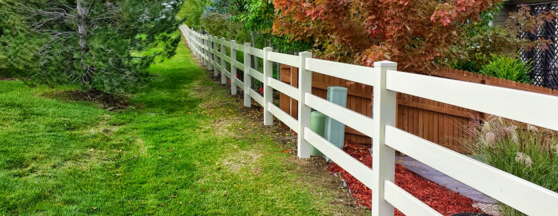 A white fence surrounds a wooden fence in a yard.