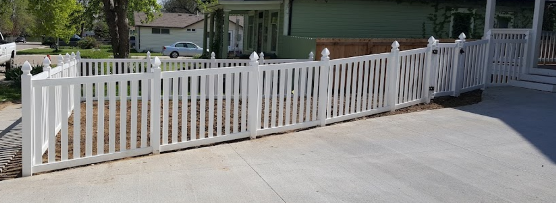 A white picket fence surrounds a driveway in front of a house.