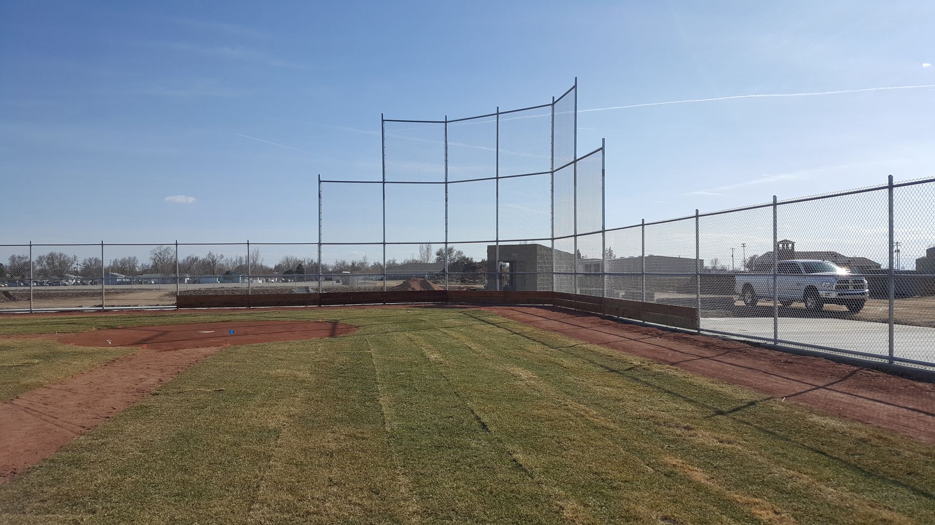 A baseball field with a chain link fencebuit by Greater Western Fence and a truck parked in the background.