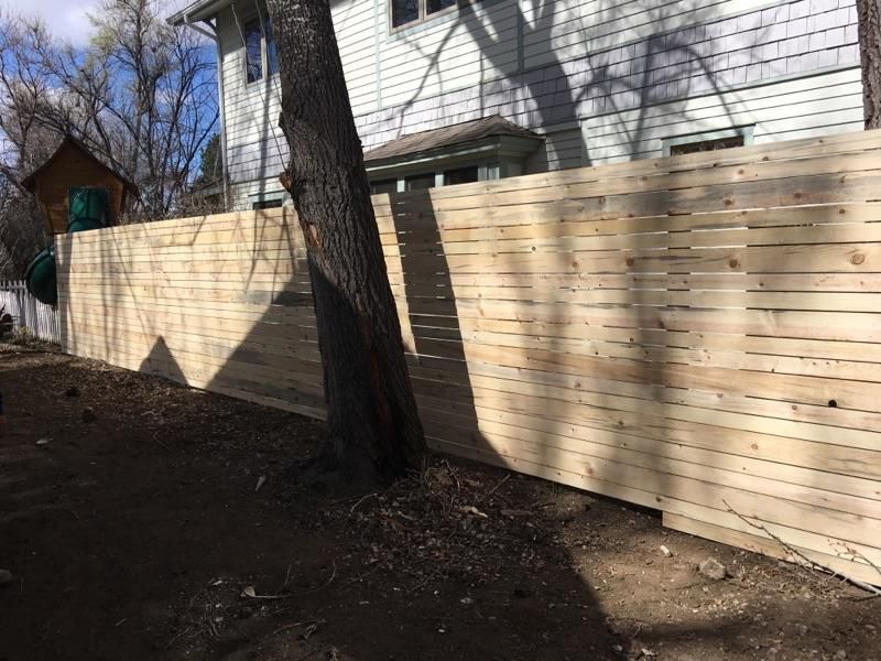 A wooden fence is in front of a white brick house.