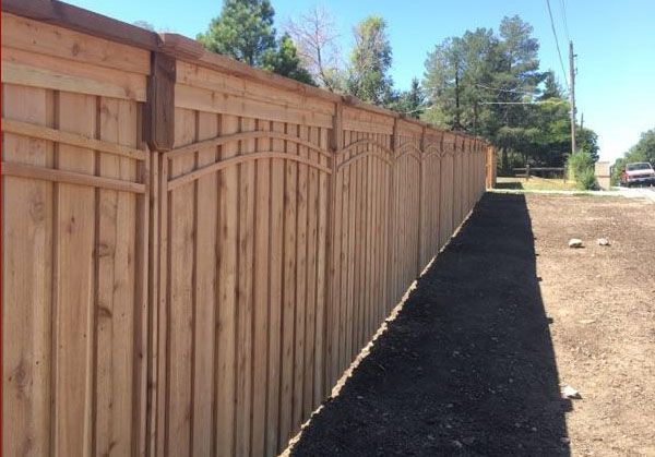 A wooden fence buit by Greater Western Fencealong a dirt road with trees in the background