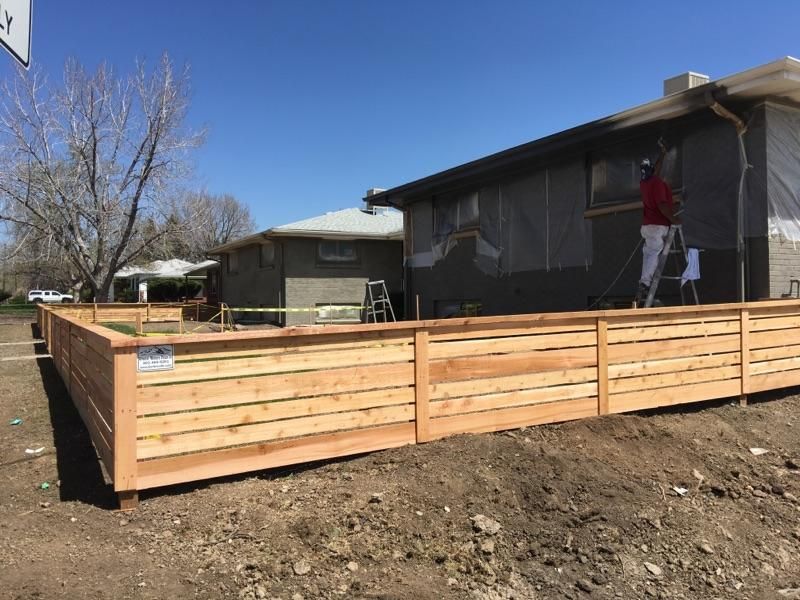 A man is painting the side of a house with a wooden fence.