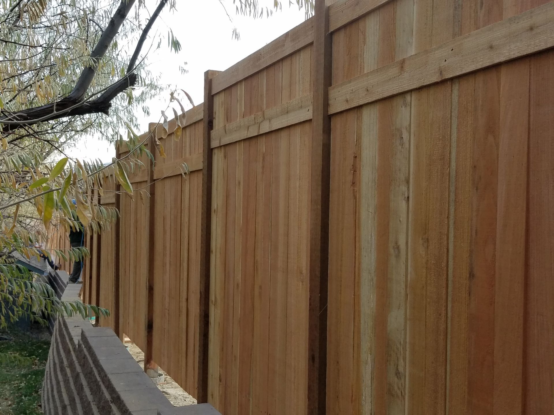 A wooden fence is surrounded by a stone wall and trees.