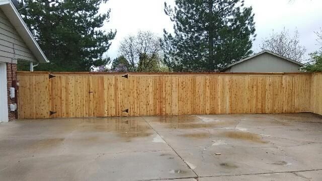 A wooden fence surrounds a concrete driveway in front of a house.