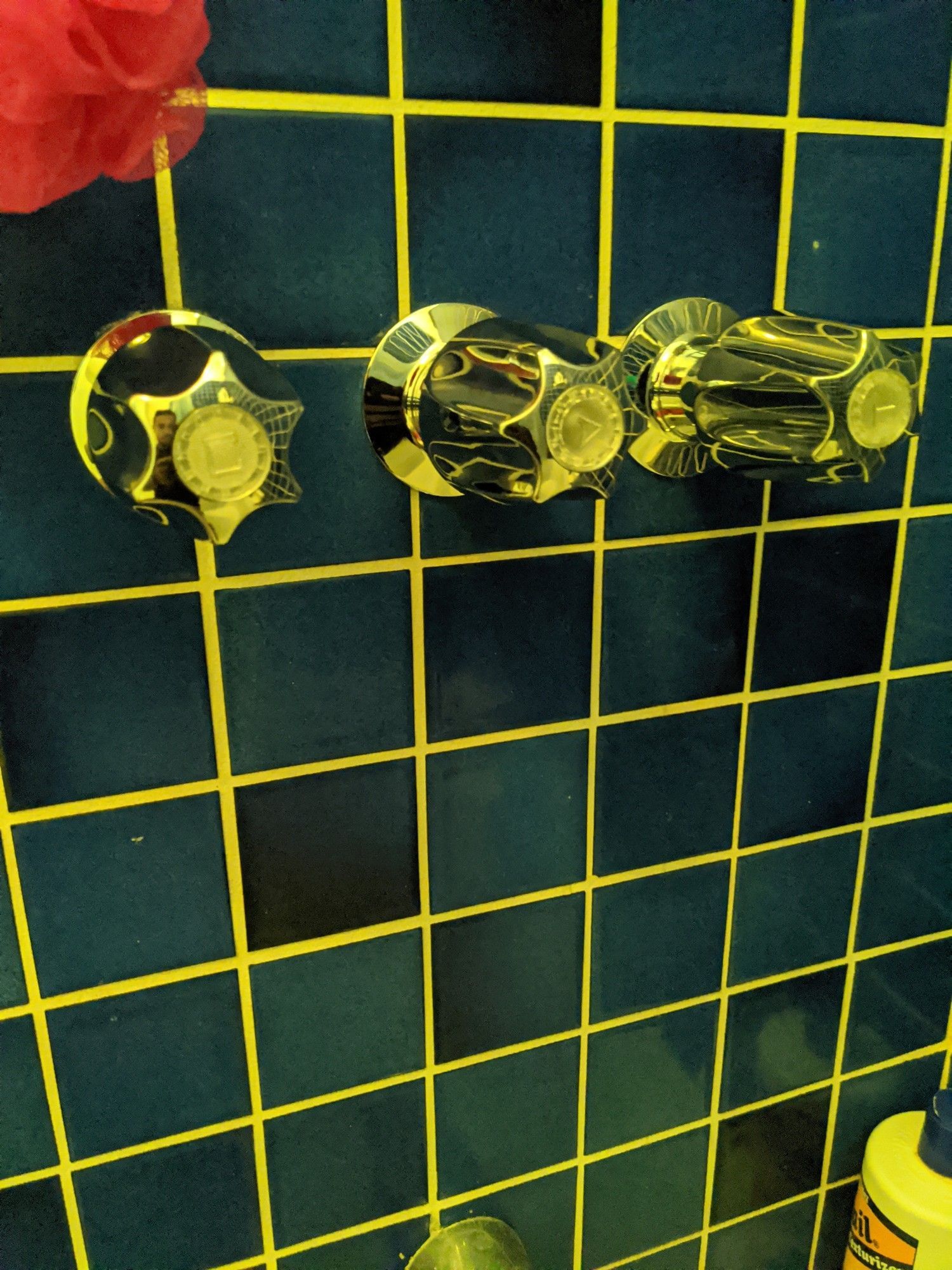 A shower head with three faucets on a blue tiled wall