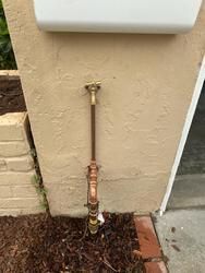 A copper pipe is attached to a wall next to a mailbox.