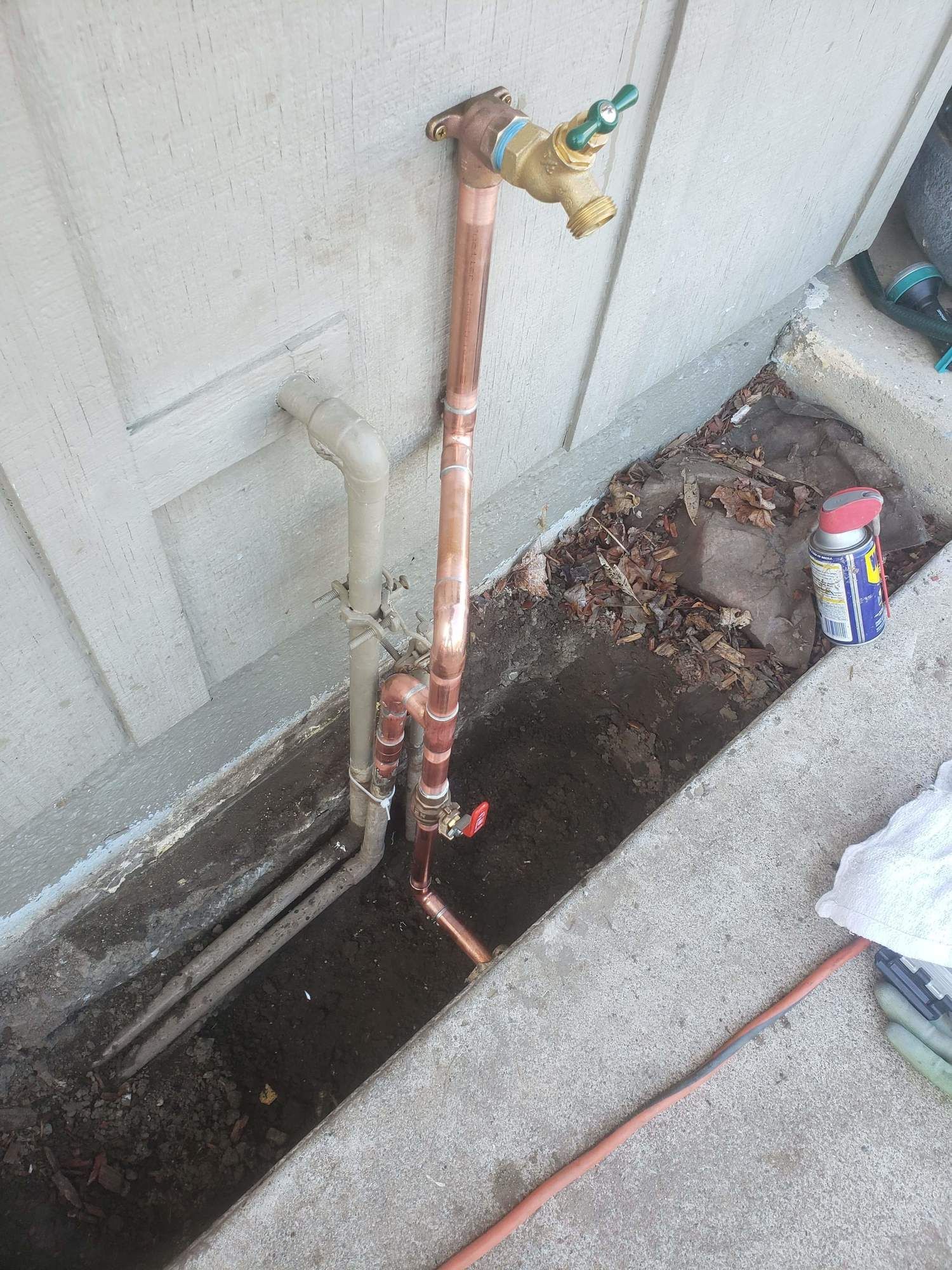 A copper pipe is connected to a faucet on the side of a building.