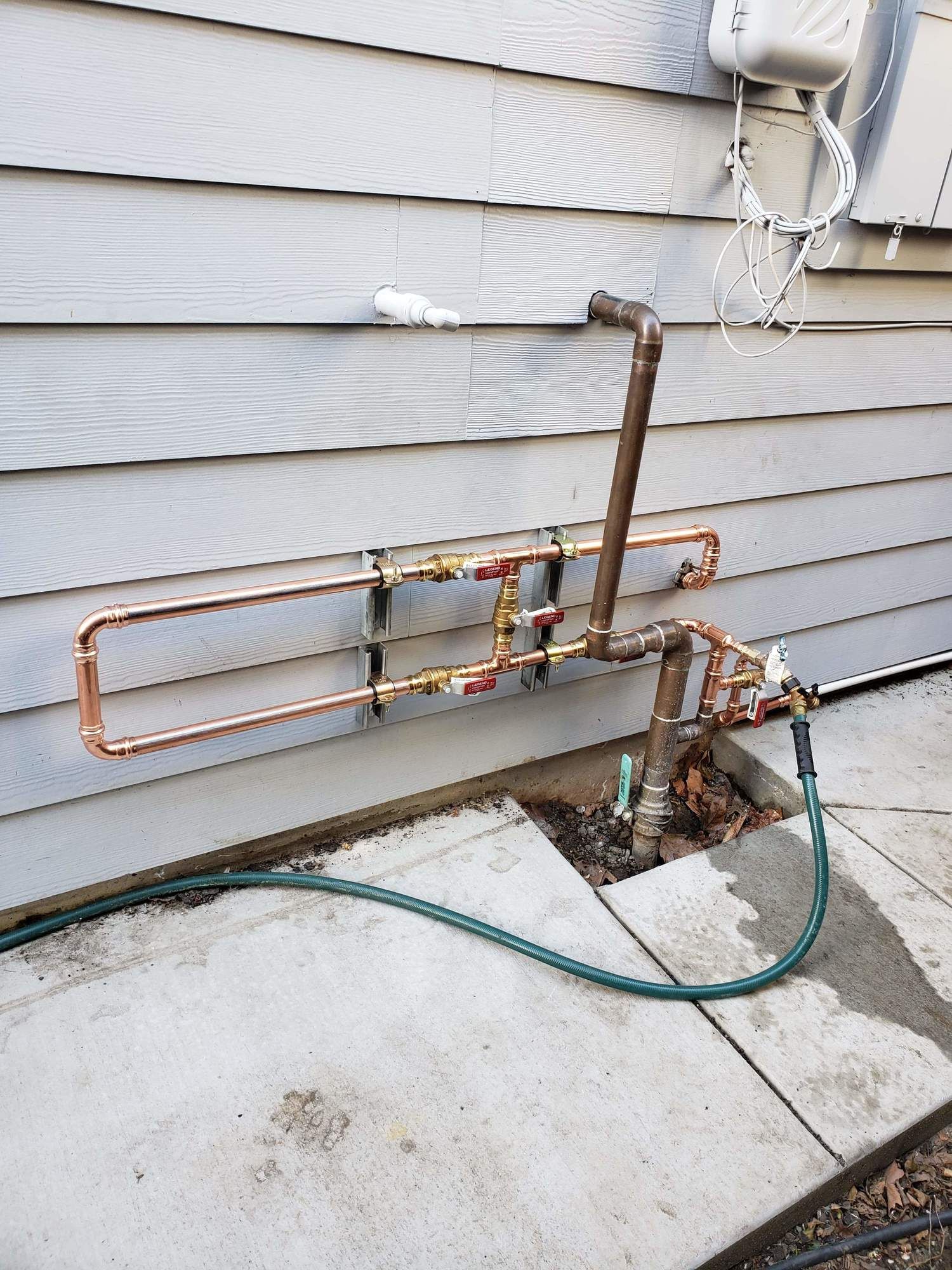 A hose is attached to a copper pipe on the side of a house.