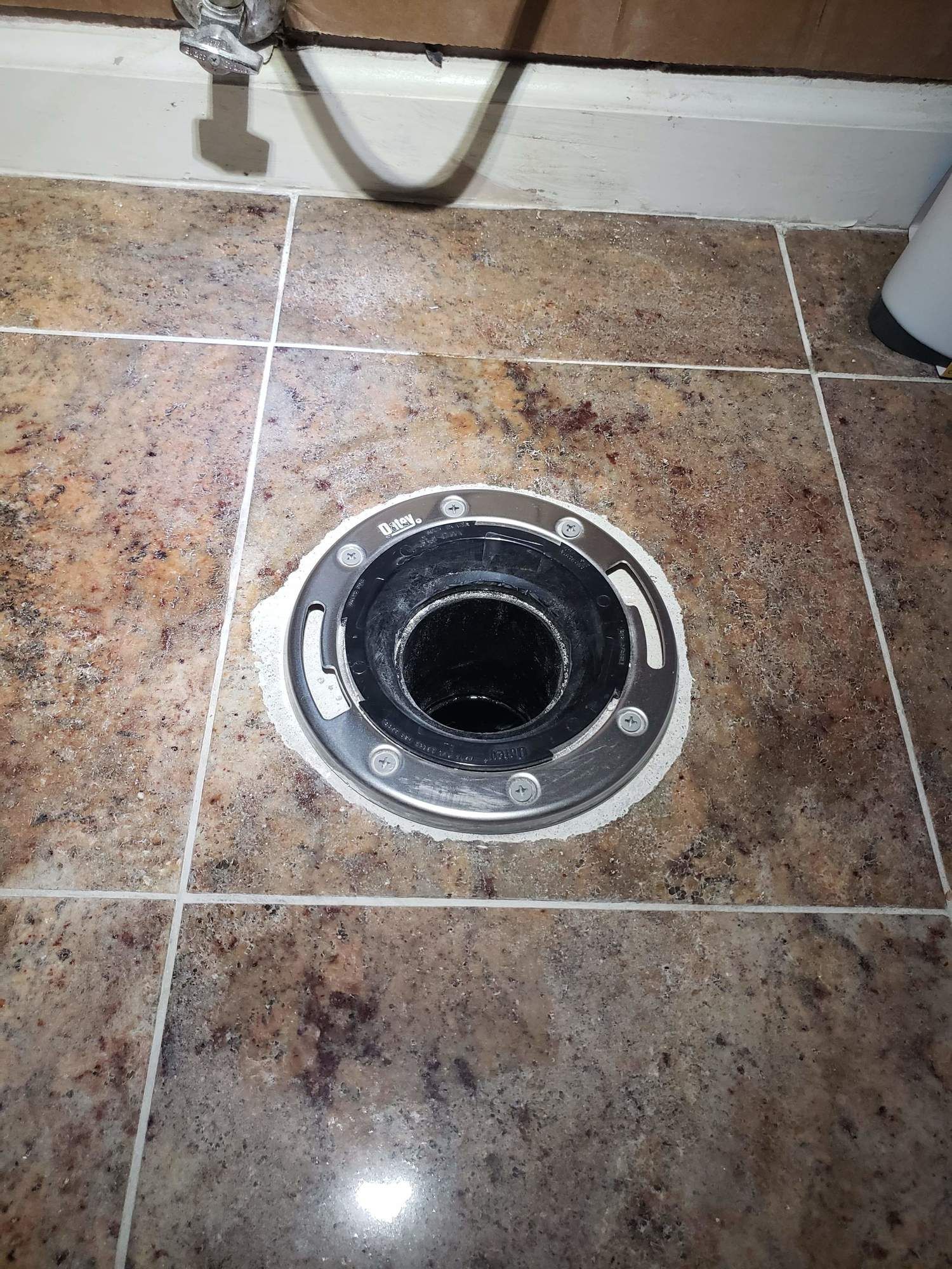 A close up of a toilet flange on a tiled floor.