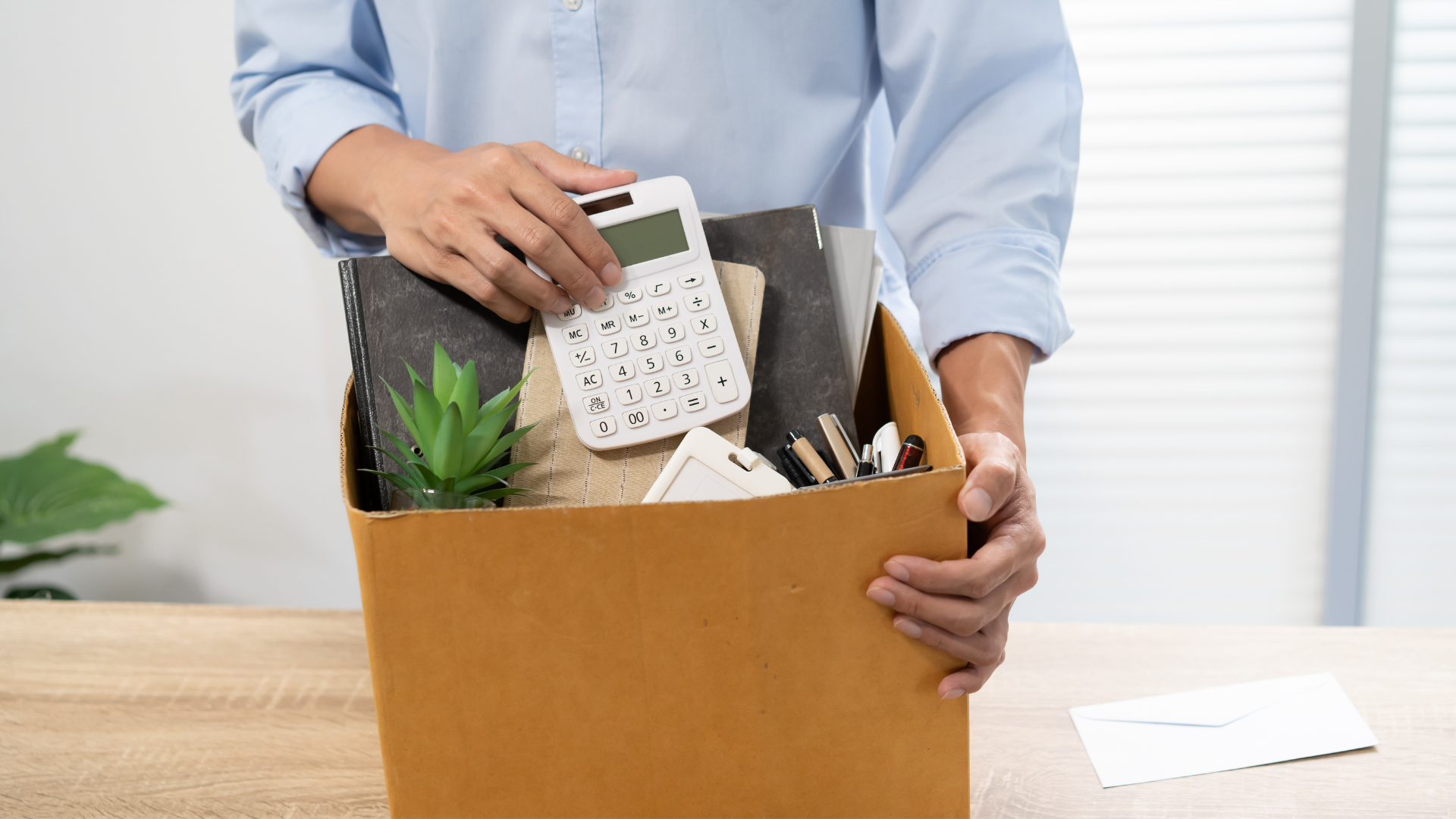 A person packing office supplies, including a calculator, notebooks, and pens, into a cardboard box