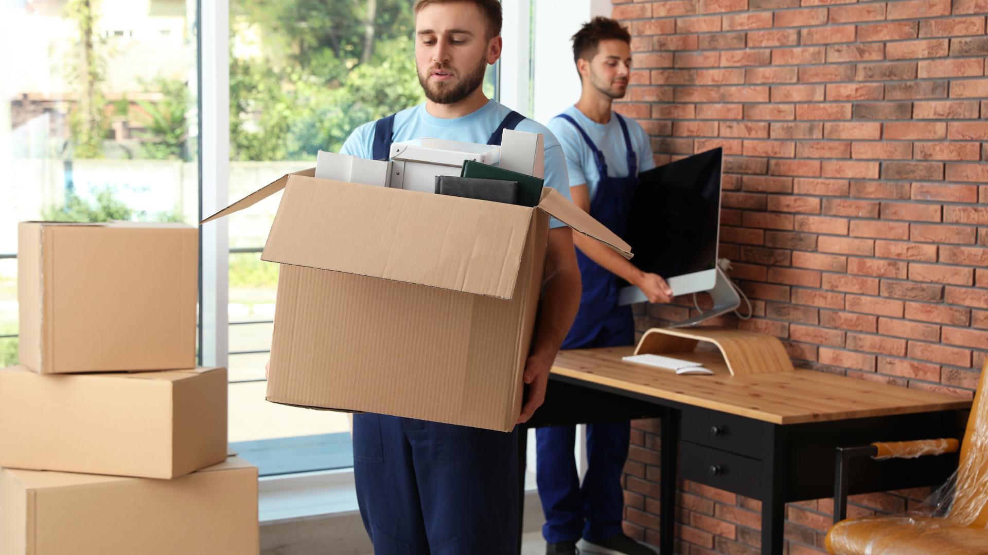 Two professional movers carrying boxes and equipment while moving into a new office space, showing t