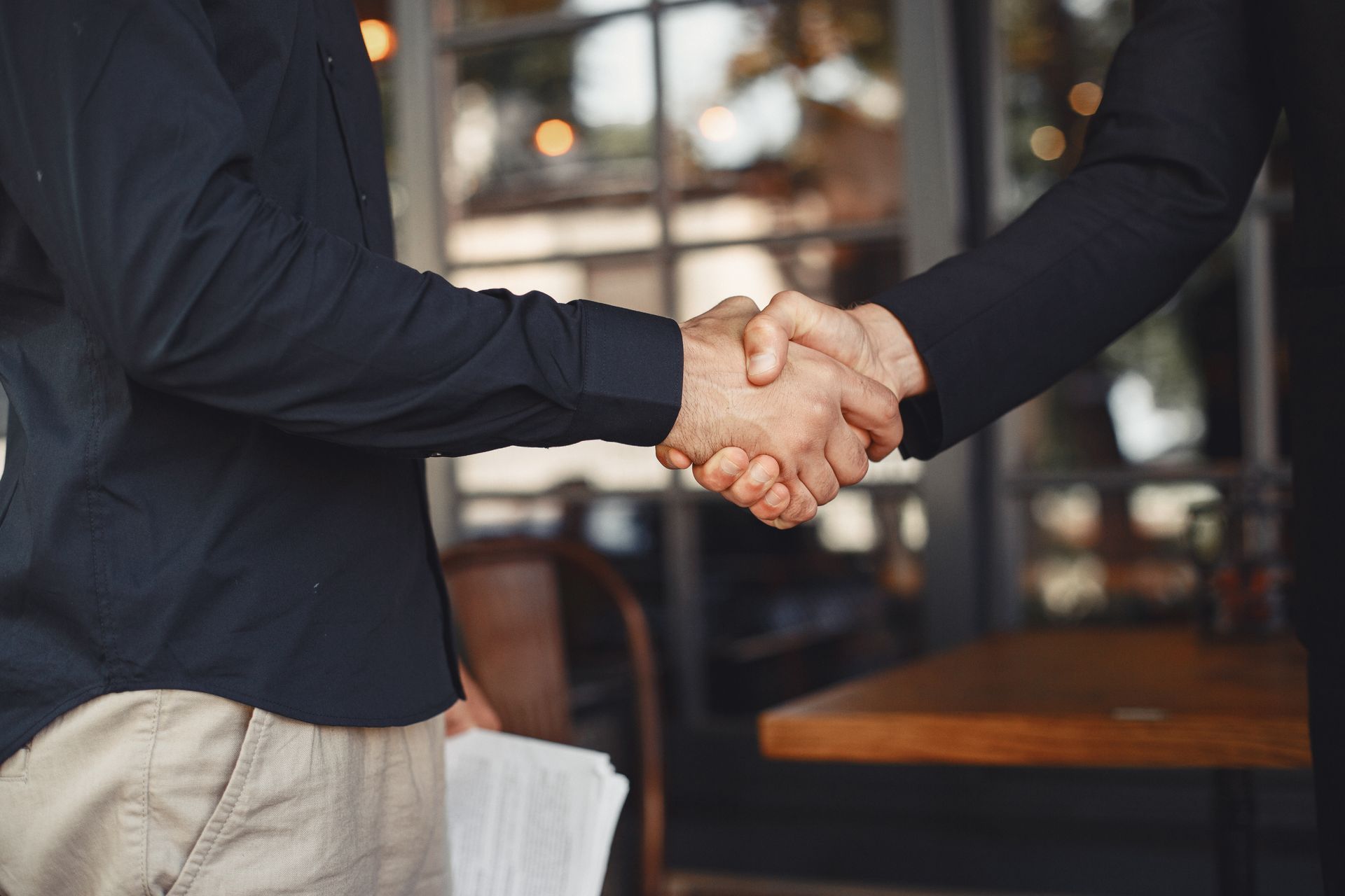 Two people shaking hands, blurred restaurant background.