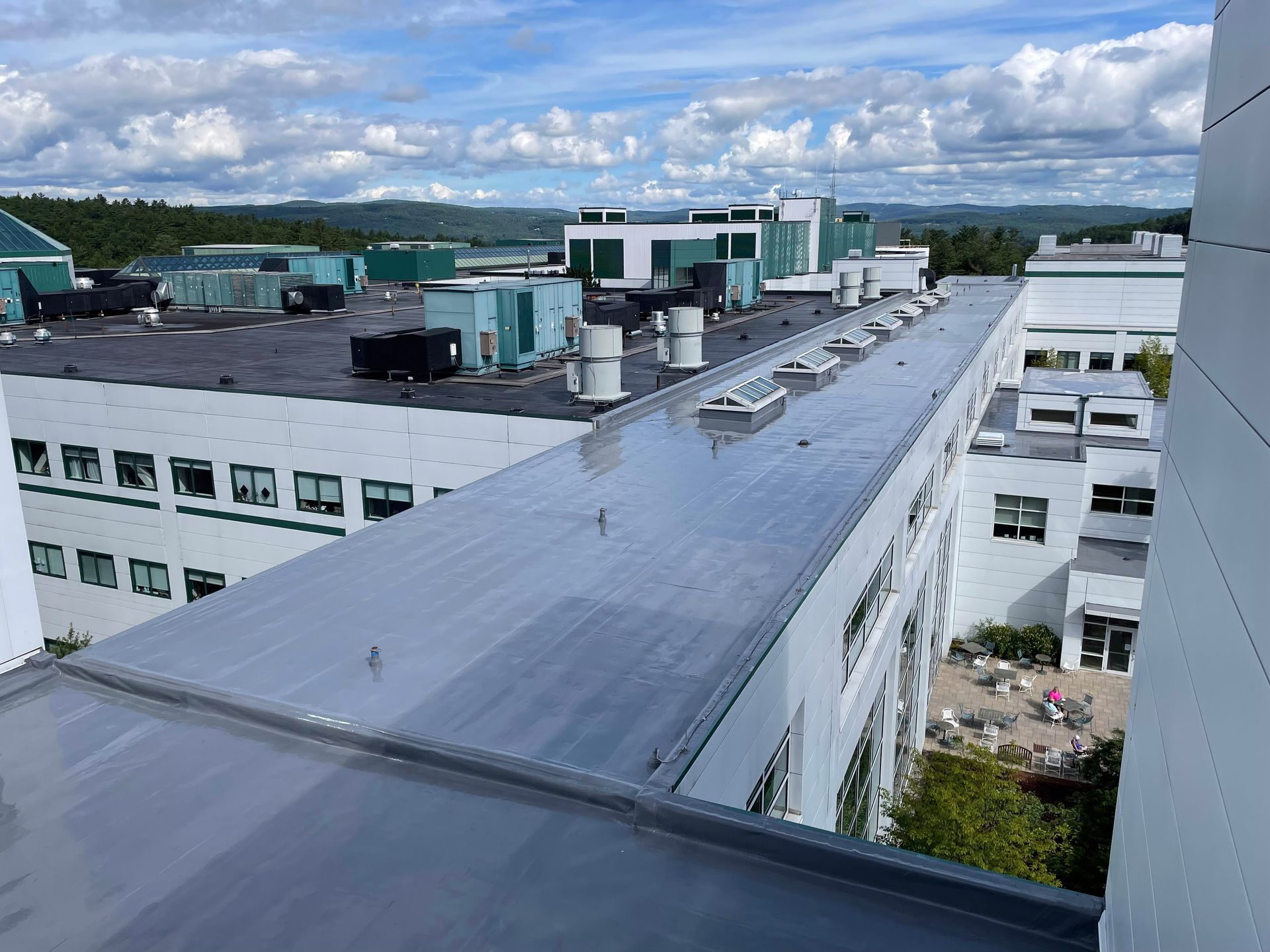 Large commercial flat roof with rooftop HVAC equipment and vents under a partly cloudy sky.
