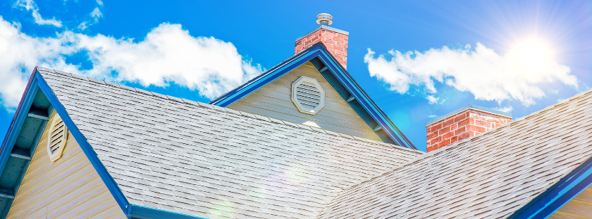 Residential shingle roof with gable vents under a bright blue sky, illustrating attic ventilation.