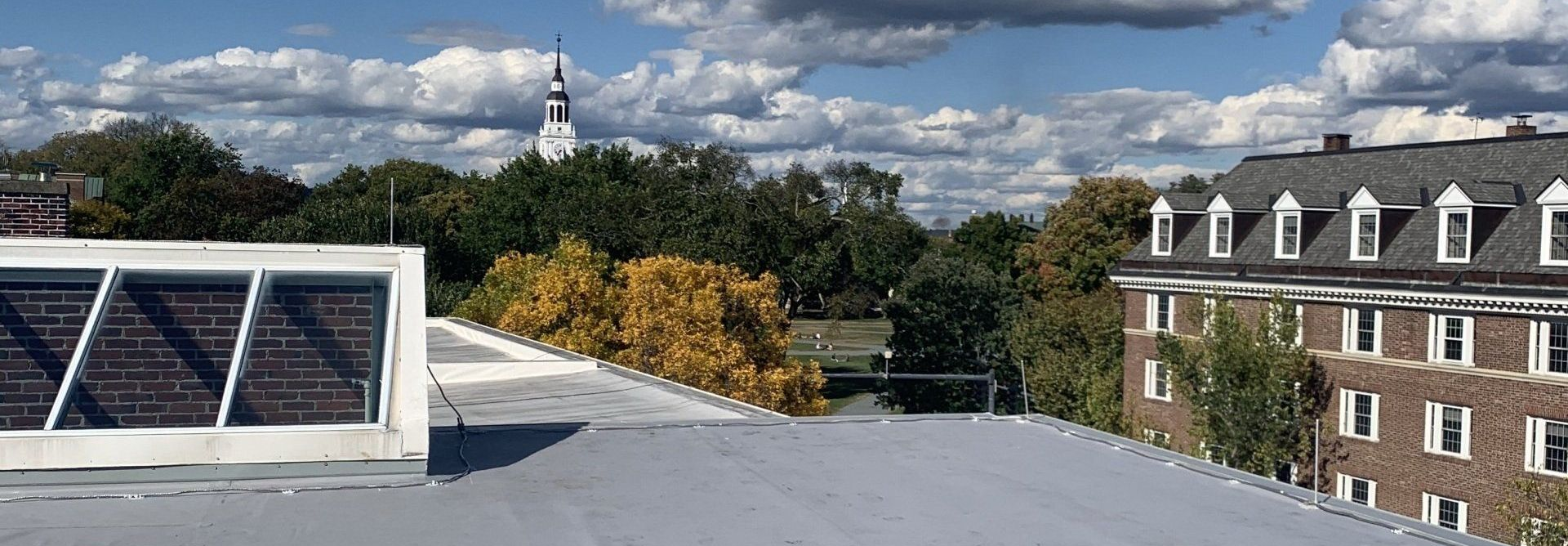 Rooftop view with solar panels, trees, a brick building, and a church steeple under cloudy skies
