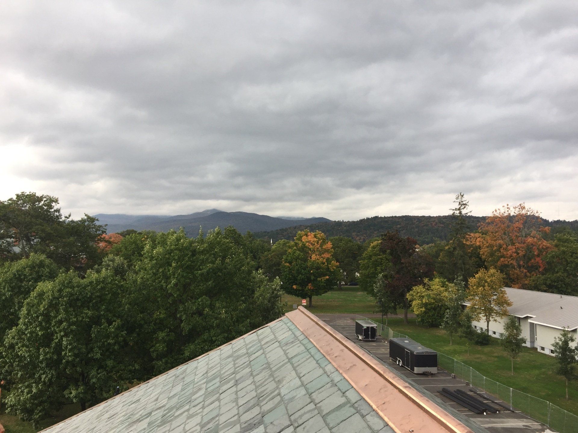 Rooftop view of cloudy sky, trees, distant hills, and houses in autumn colors